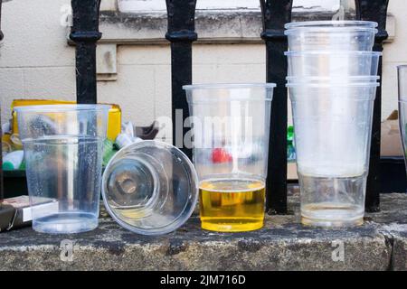 Un gros plan de gobelets en plastique et en verre sur la surface du mur de briques contre les rails métalliques. Banque D'Images