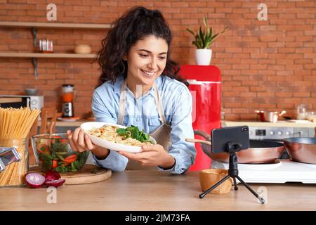 Jeune femme avec des pâtes savoureuses enregistrement vidéo cours dans la cuisine Banque D'Images