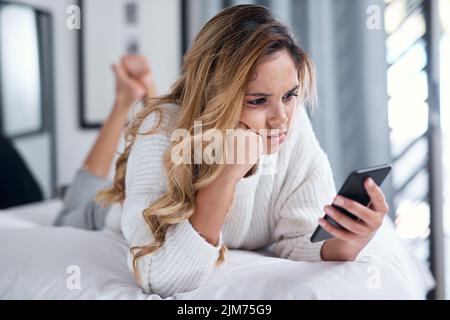 Un autre jour de défilement dans mon fil d'actualité, une jeune femme utilisant son téléphone portable en étant couché sur son lit. Banque D'Images