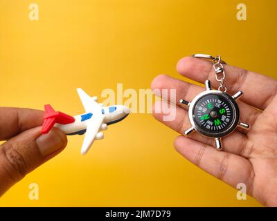 Mains adultes tenant des jouets avion et boussole porte-clés isolé sur un fond jaune.concepts de vacances et de voyage. Banque D'Images