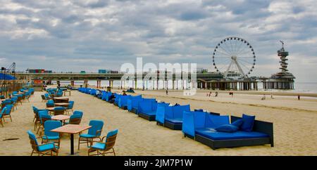 Terrasse de café sur la plage de Scheveningen sans consommateur. Il y a une jetée avec une grande roue de ferris et une tour sur elle en arrière-plan Banque D'Images