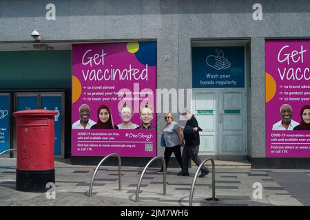 Slough, Berkshire, Royaume-Uni. 4th août 2022. Les acheteurs marchent devant le nouveau rose fluo reçoivent des panneaux de vaccination à Slough High Street. Le Comité mixte sur la vaccination et l'immunisation (JCVI) a récemment annoncé que toutes les personnes âgées de 50 ans et plus seront parmi celles qui se verront offrir un rappel COVID-19 et un jab de la grippe cet automne dans le cadre de plans visant à accroître la protection contre les virus respiratoires en prévision de l'hiver. Crédit : Maureen McLean/Alay Live News Banque D'Images