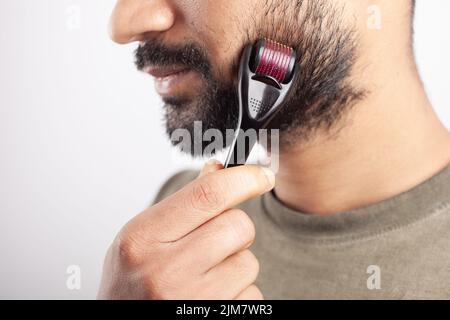 Beau type utilisant dermaroller pour la croissance de la barbe sur fond blanc Banque D'Images