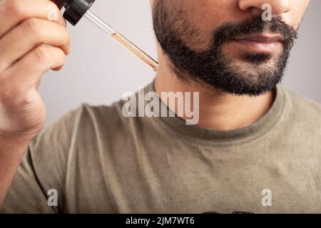 gros plan d'un homme tenant un compte-gouttes rempli de minoxidil qui va s'appliquer à la croissance de la barbe isolée sur fond blanc. Banque D'Images