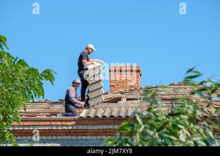 Région de Krasnodar. Russie. 15 juillet 2022. Les travailleurs sur le toit d'un bâtiment sont en train de démanteler de vieilles feuilles d'ardoise d'amiante. Les couvreurs réparent le toit. Banque D'Images