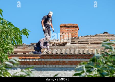 Région de Krasnodar. Russie. 15 juillet 2022. Les couvreurs sur le toit d'un bâtiment retirent les anciennes feuilles d'ardoise d'amiante. Les travailleurs réparent le toit. Banque D'Images