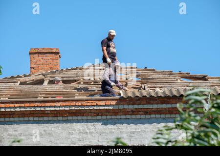 Région de Krasnodar. Russie. 15 juillet 2022. Les travailleurs sur le toit du bâtiment sont en train de démanteler de vieilles feuilles d'ardoise. Les couvreurs réparent le toit. Banque D'Images