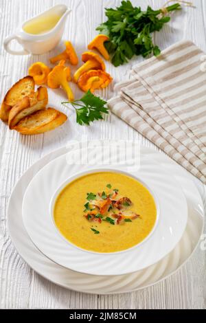 Soupe de crème chanterelle dans un bol blanc sur une table en bois blanc avec des ingrédients, vue verticale depuis le dessus Banque D'Images