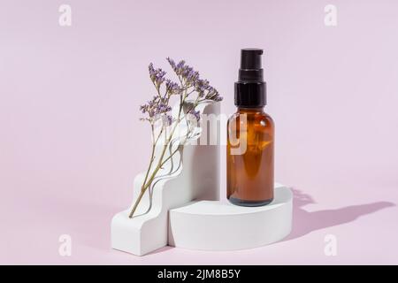 Flacon compte-gouttes en verre ambré sur podium blanc et formes géométriques et fleur pourpre sèche sur fond rose clair. Produits de soin de la peau, cosmétiques naturels. C Banque D'Images