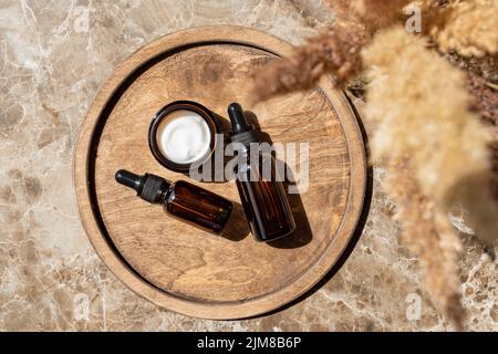 Ensemble de bouteilles de cosmétiques en verre ambré sur plateau en bois. Bouteille compte-gouttes et emballage de pots de crème. Soin de la peau produits de beauté emballage design pour la routine quotidienne. Banque D'Images