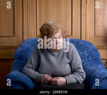 La vieille femme est assise dans un fauteuil Banque D'Images