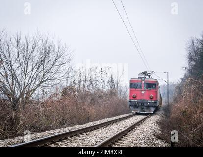 Vue sur la ligne de chemin de fer en hiver. Une vieille locomotive électrique sur une voie ferrée couverte de brouillard d'hiver de jour. Le concept de voyager en train. Banque D'Images