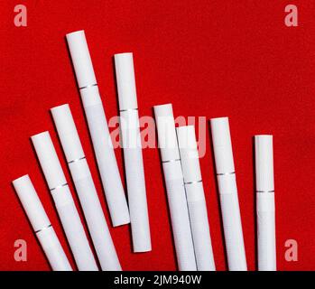 Cigarettes blanches dispersées sur fond rouge Banque D'Images