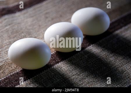 trois œufs blancs regroupés sur le dessus du tissu et l'éclairage latéral doux - mise au point sélective Banque D'Images