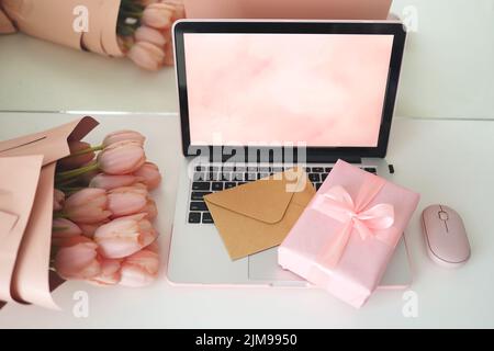Espace de travail féminin avec tulipes roses, ordinateur portable et enveloppe. Vue de dessus de l'écran de l'ordinateur portable. Boîte cadeau rose et souris d'ordinateur rose. Banque D'Images