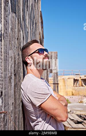 Homme caucasien barbu en lunettes de soleil rester près du mur en bois à l'extérieur.Concept d'auto-isolement pendant la quarantaine du coronavirus Banque D'Images