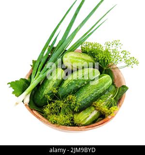 Concombres et légumes et feuilles d'aneth encore vie dans un bol en bois isolé sur fond blanc. Banque D'Images