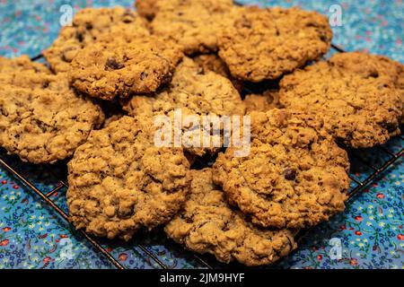 Biscuits aux pépites de chocolat faits maison sur une grille de refroidissement avec une nappe à fleurs bleues en dessous. Banque D'Images