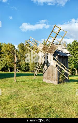 Un vieux moulin à vent en bois et une croix se tiennent sur un pré vert par temps ensoleillé et clair contre un ciel bleu. Espace de copie, image verticale. Banque D'Images