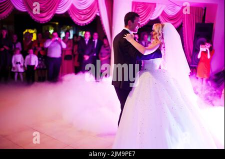 Première danse de mariage étonnant de jeunes mariés en faible lumière rose et la fumée intense Banque D'Images