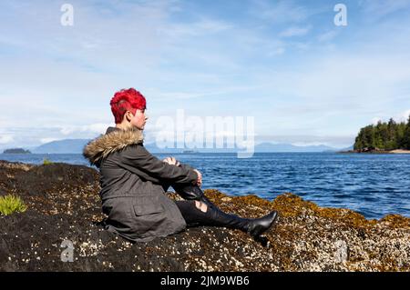 Jeune fille pensant tout en étant assis sur le rocher près du lac et des bois Banque D'Images