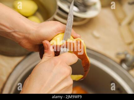 Femme coupant pour peler les pommes de terre. Cuisine. Préparez les aliments Banque D'Images