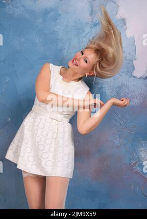 Photomodel blond à longues pattes, en mini-drase blanc et bas blancs posant au studio. Un sourire magnifique, une jambe incroyable Banque D'Images