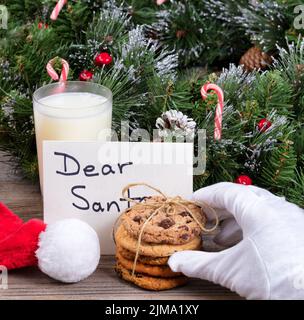 Main du Père Noël atteignant un cookie avec des décorations de vacances et une carte en arrière-plan Banque D'Images