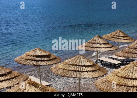 Plage de galets vide avec parasols en osier et chaises longues. Vue pittoresque sur la mer avec de l'eau bleue, station d'été Banque D'Images