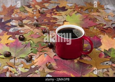 Grande tasse rouge de café chaud foncé et de feuilles d'automne sur des panneaux de bois rustiques Banque D'Images