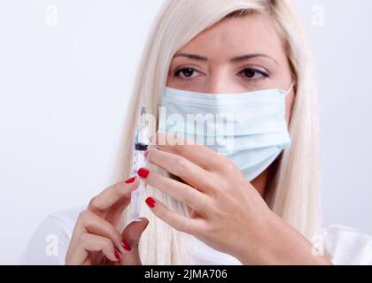 Femme médecin ou infirmière dans un masque médical tenant une seringue avec injection, vaccin contre le virus corona Banque D'Images