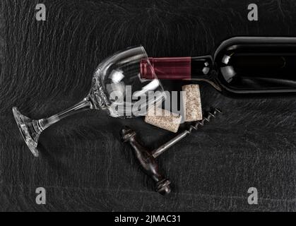 Vue en hauteur d'un tire-bouchon vintage avec une bouteille de vin rouge et un verre sur fond d'ardoise noire Banque D'Images