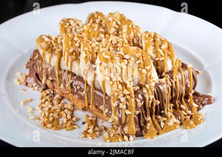 Gaufres belges au chocolat blanc. Croissant gaufré ou croffe avec garniture au chocolat servi dans un plat et fond noir. Banque D'Images