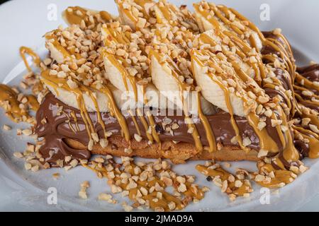 Gaufres belges au chocolat blanc. Croissant gaufré ou croffe avec garniture au chocolat servi dans un plat et fond noir. Banque D'Images