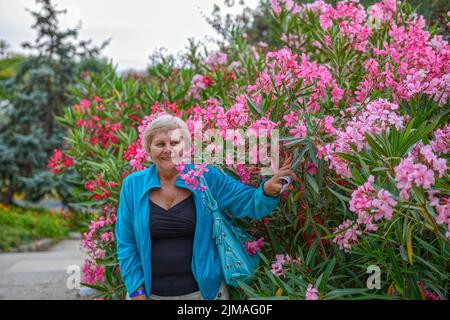 Gros plan portrait d'une femme âgée souriante qui pose près d'un buisson à fleurs dans le parc Güell, Barcelone. Banque D'Images