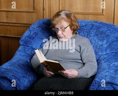 La vieille femme est assise dans un fauteuil et lit le livre Banque D'Images