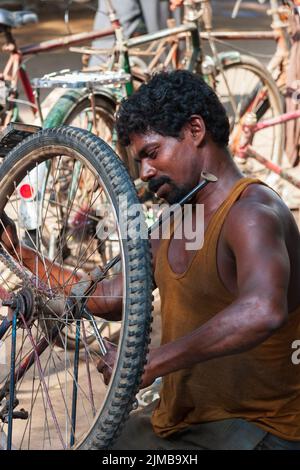 Un Indien utilise une clé pour serrer la vis sur la roue d'une bicyclette dans le centre-ville de Chennai. Banque D'Images