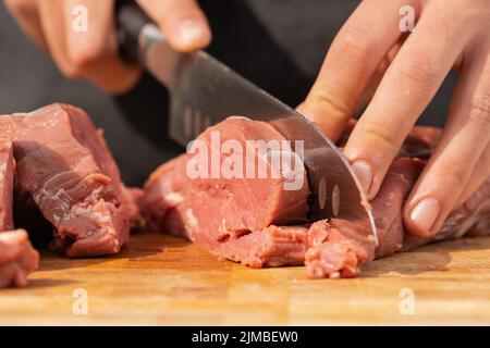 Vue rapprochée d'un homme coupant de la viande en tranches à l'aide d'un couteau sur une planche en bois Banque D'Images