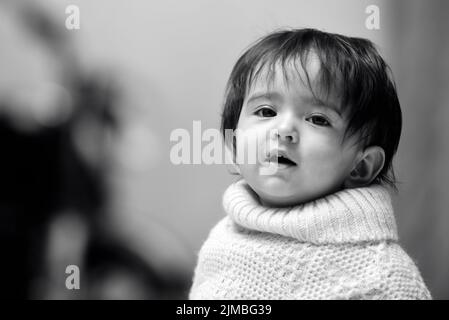 Photo en niveaux de gris d'une adorable petite fille indienne de 13 mois portant un poncho Banque D'Images
