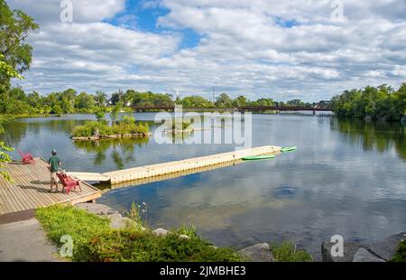 Vue panoramique de Little Lake avec des gens qui se détendent sur le pont de la jetée depuis le parc Millenium à Peterborough, Ontario, Canada Banque D'Images