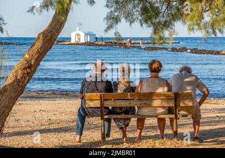 quatre retraités plus âgés assis dans le sahde d'un arbre donnant sur la mer sur l'île grecque de crète, deux couples assis sur un banc en bois Banque D'Images