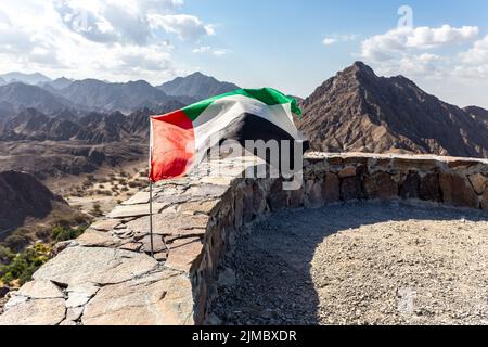 Drapeau national des Émirats arabes Unis agitant sur le vent, attaché à un mur de pierre au sommet de l'escalier de Wadi Shawka, avec les montagnes Al Hajar. Banque D'Images