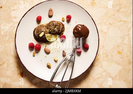 Pelle en métal remplie de sorbet au chocolat sans produits laitiers et de boules de chocolat surgelées sur plaque blanche sur fond de marbre Banque D'Images