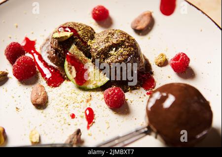 Pelle en métal à vie avec glace au chocolat, garnie de framboises, de fèves de cacao et de confiture de baies sur une assiette blanche Banque D'Images