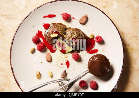 Plat de pelle en métal avec glace au chocolat, garni de framboises, de fèves de cacao et de confiture de baies sur une assiette blanche Banque D'Images