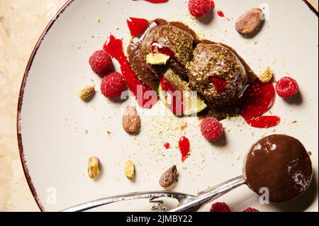 Vue de dessus d'une pelle en métal pour sorbet, avec glace au chocolat maison, sans lait, garnie de pistaches râpées, framboises, fèves de cacao et d'être Banque D'Images