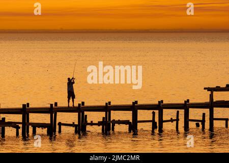 Un pêcheur jette sa ligne d'un quai à Fairhope, Alabama, au coucher du soleil dans une image composite. Banque D'Images