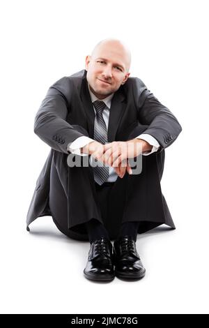 Charmant homme d'affaires souriant dans un costume noir assis au sol Banque D'Images