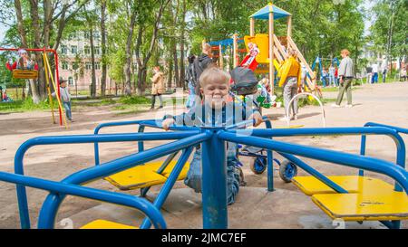 Un garçon blond de trois ans dans un parc de loisirs se déplace sur un carrousel mécanique pour enfants. Couleur d'ambiance - Bleu Banque D'Images