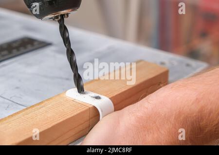 Un homme fore des trous dans un crochet en fer avec une perceuse pour accrocher un écran en bois sur une batterie. Banque D'Images